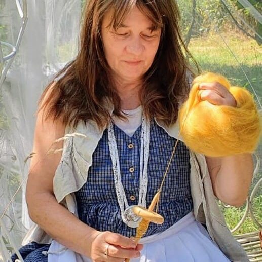 Petra Voß sitzt und spinnt gelbe Wolle mit einer Handspindel