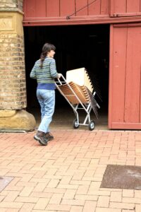 Ein Stapel Stühle wird mit dem Stuhlwagen in die Deele geschoben